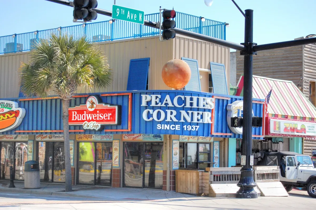 An exterior shot of Peaches Corner’s colorful signage and vibrant façade, with palm trees and a lively street scene. The image exudes local flavor and hints at the variety of entertainment, dining, and people-watching experiences available nearby.