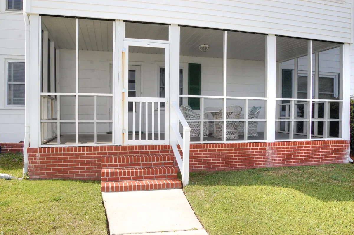 An inviting screened porch with brick steps and wicker chairs, offering a comfortable spot to relax, socialize, or read while enjoying the fresh sea breeze and views of the outdoors.