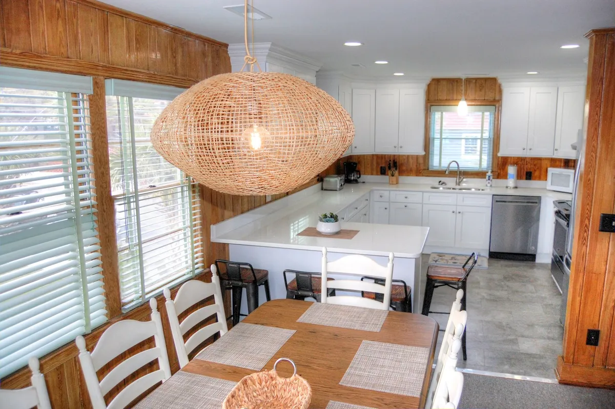 A kitchen and dining space featuring a large woven pendant light, an inviting dining table, and a spacious kitchen island. The area is set for both cooking and hosting, reflecting warmth and togetherness.