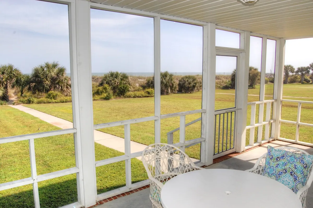 A relaxing screened-in porch with a table and chairs positioned to take in the landscape, likely with glimpses of sunrise or sunset. The scene evokes leisure and socializing in a protected, airy outdoor space.