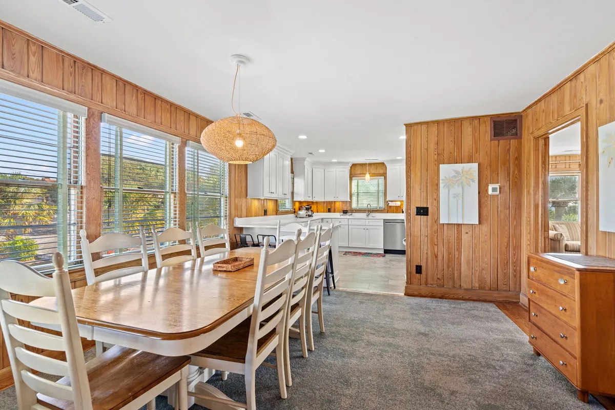 An open-concept dining and kitchen area featuring a welcoming dining table, stylish light fixture overhead, and wood accents. The kitchen is easily visible from the dining area, emphasizing the flow between cooking and socializing spaces.