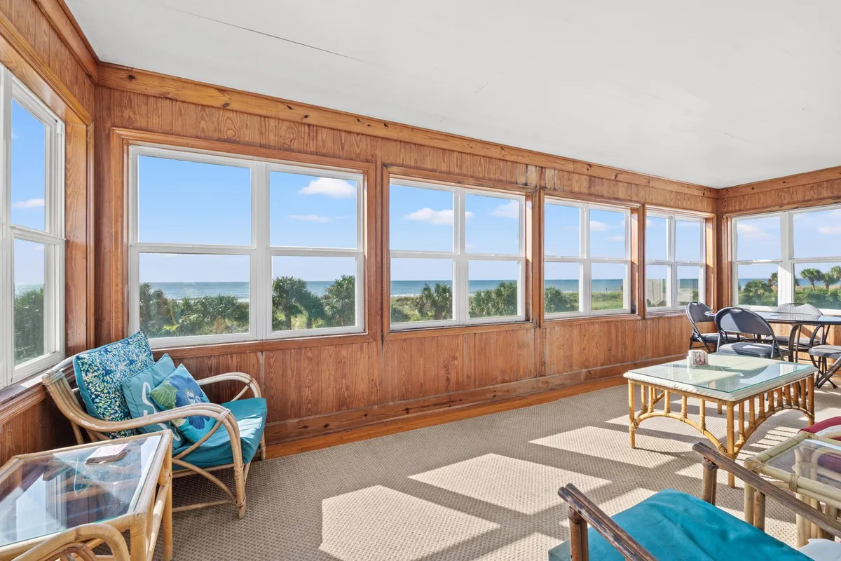 A serene and airy sunroom with large windows offering sweeping views, comfortable seating accented with colorful cushions, and glass-topped tables. The abundance of natural light and vistas make it an ideal spot for sunrise coffee or relaxing with friends and family.